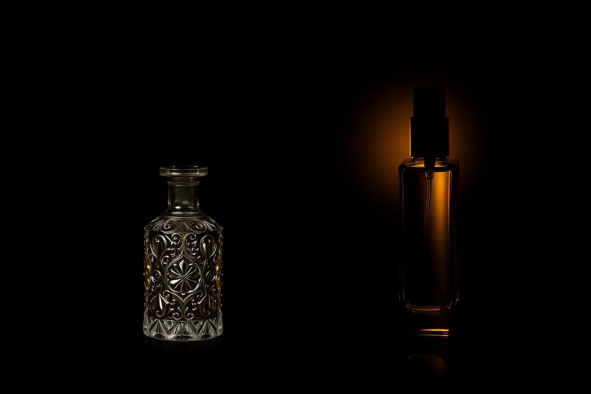 Traditional attar bottle beside a modern perfume spray bottle in deep shadow